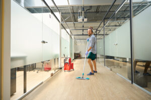 Cheerful informal mopping the floor in the office hallway, he works to music, uses a headset