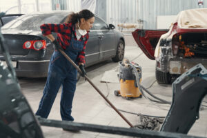 Serious woman using mop while washing floor at service station