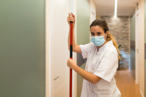 Young woman wearing her uniform and a face mask holding mop in clinic.